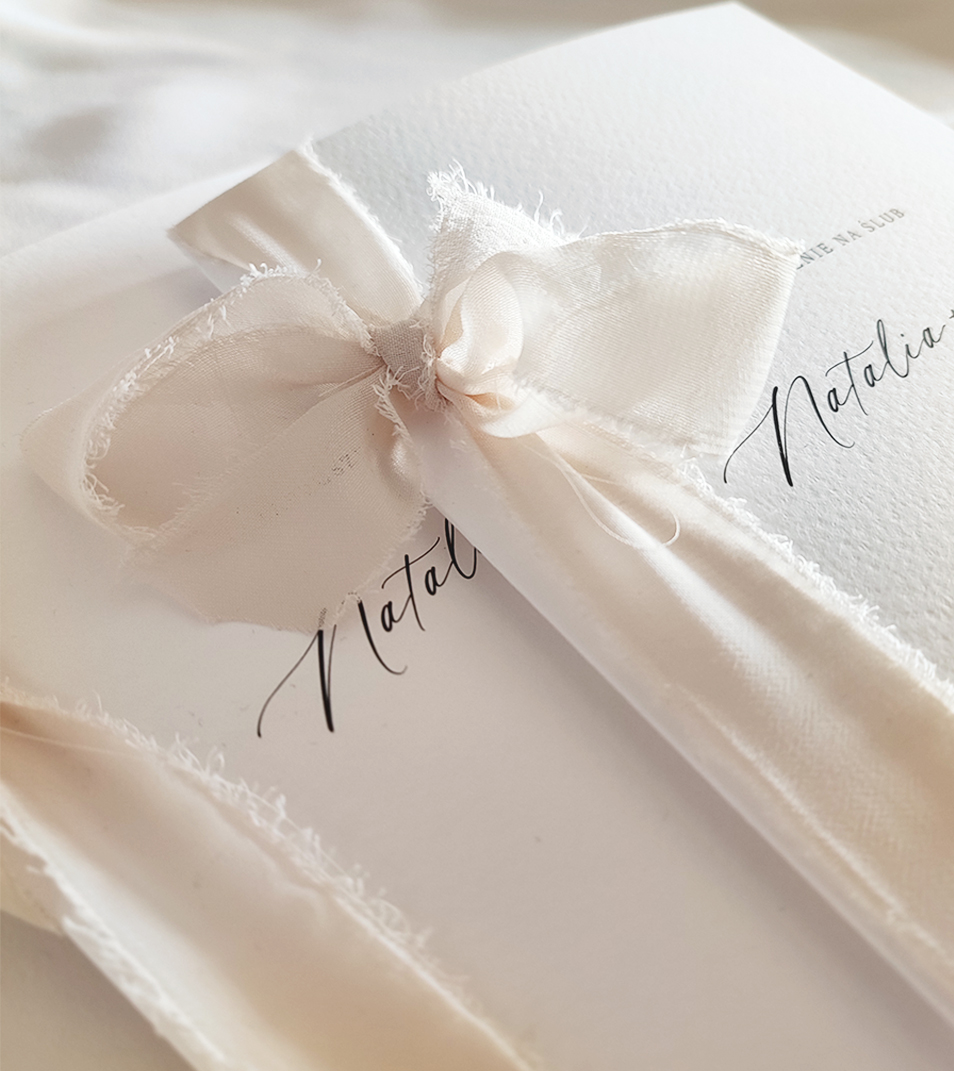 Beżowa wstążka szyfonowa wiązana w kokardkę w zaproszeniach ślubnych.